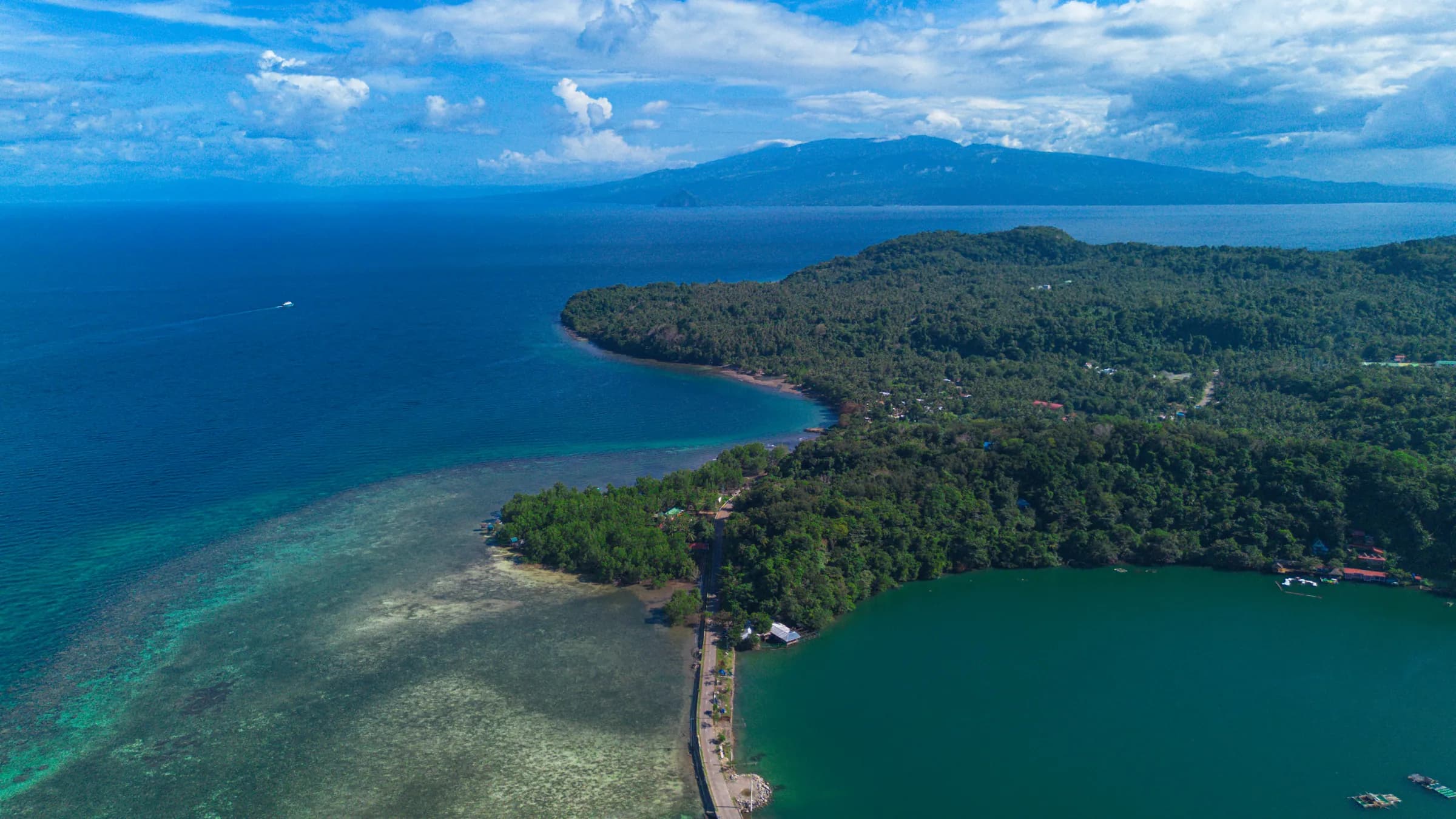 Camiguin's coastline from the air, the ring road threading between the volcanic headlands and the Bohol Sea